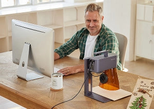工房でLaserPecker LP4が製品を加工する間、パソコンでオリジナル商品のデザインを作成する小規模事業者。